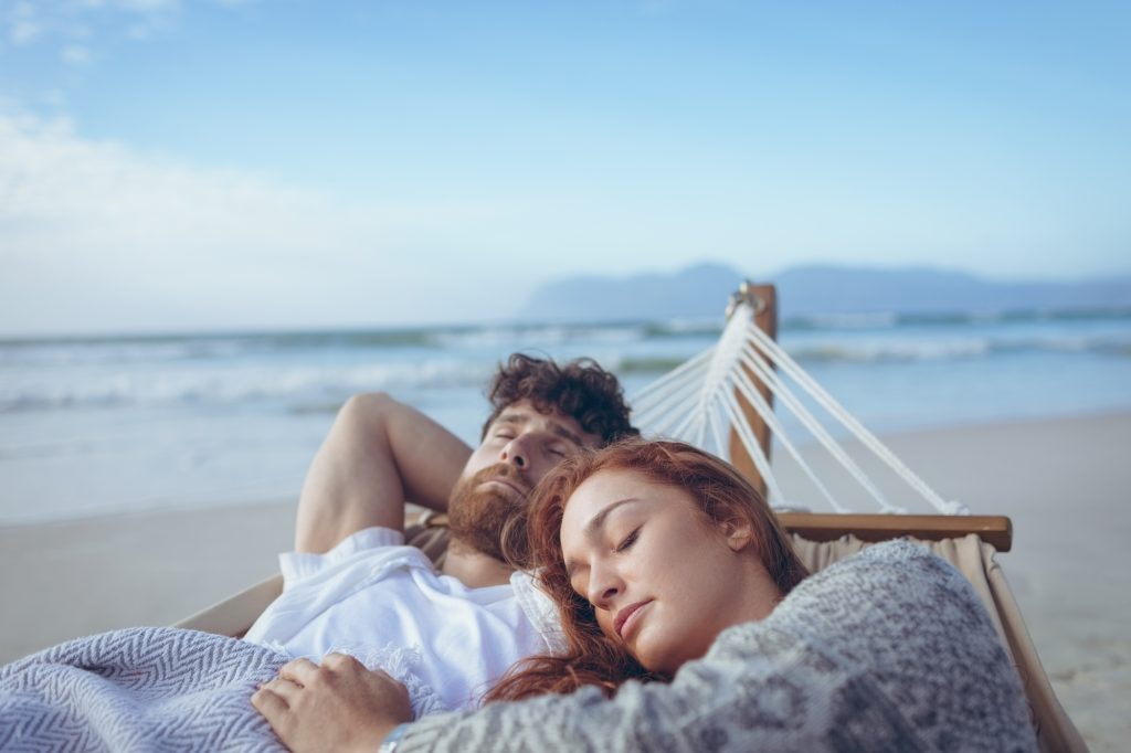 Front view of relaxed Caucasian couple sleeping on hammock at beach. Ocean in the background
