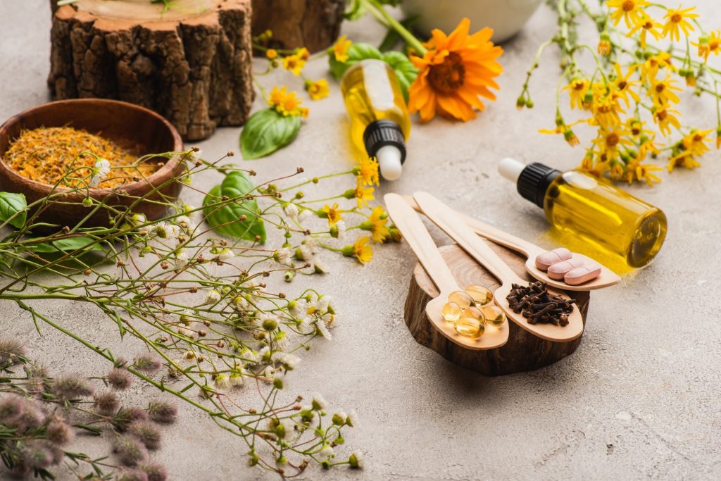 selective focus of wildflowers, herbs, bottles and pills in wooden spoons on concrete background,